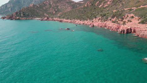 vista de drones cerca de la costa de montañas rojas y vegetación verde en el mar azul tropical con olas rompiendo en las rocas en cerdeña, italia - tiro aéreo