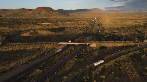 Vista-Aérea-Del-Tráfico-Ligero-En-La-Interestatal-40-Y-El-Paso-Elevado-De-La-Autopista-93-Cerca-De-Kingman-Arizona-Al-Atardecer,-Montañas-En-El-Fondo,-Hora-Dorada