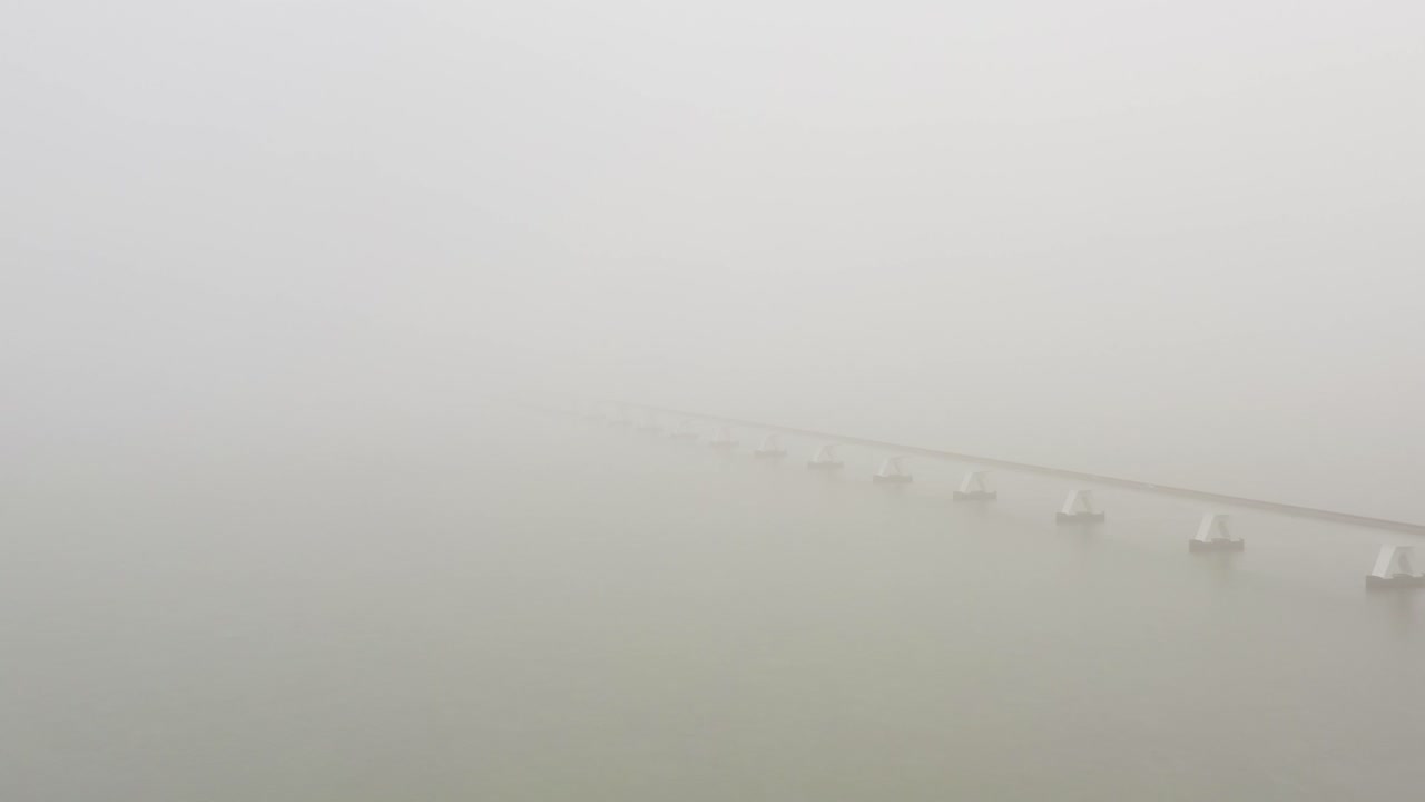Drone shot of a long bridge crossing between islands during thick fog in the Netherlands. High angle