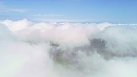 descend aerial drone flight through white clouds revealing green farm fields in the valley