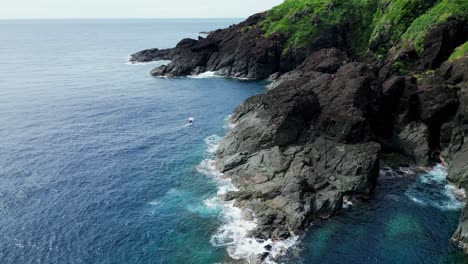 Orbiting-Aerial-View-of-stunning-turquoise-ocean-waves-crashing-against-tropical-island-rock-formation-within-lagoon-in-Catanduanes,-Philippines