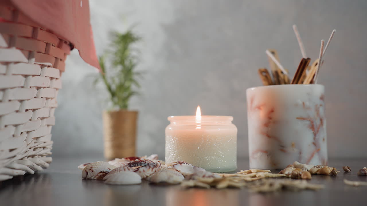 Une bougie blanche émet une douce fumée après que la flamme s’est éteinte, entourée de coquillages, d’étoiles de mer, de coquilles d’escargots, d’un panier décoratif en osier et d’une plante sur une table en marbre foncé