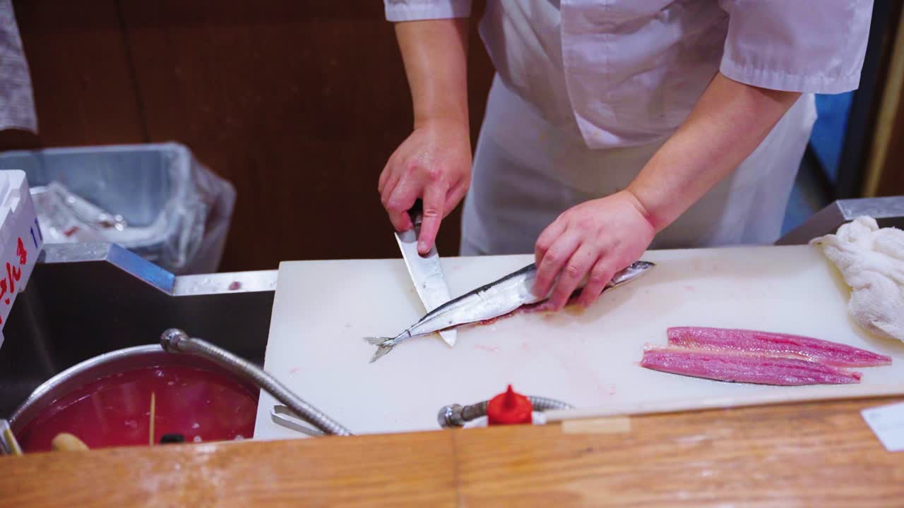 Sushi-Koch bereitet Sashimi mit Pazifischem Makrelenhecht (Sanma) für ein Omakase-Menü zu