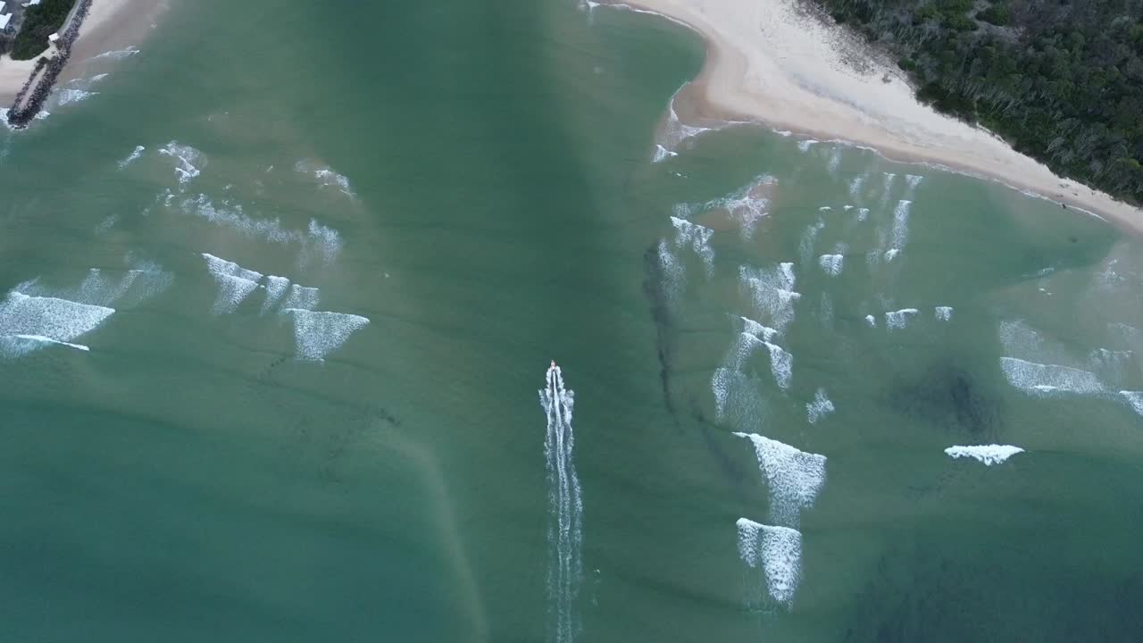 Aerial footage of a boat gliding past the golden sandy dunes at Noosa Spit, Queensland. The drone captures the crystal-clear water and the natural beauty of this iconic Australian coastal spot.