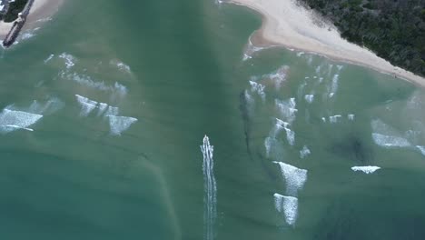aerial footage of a boat gliding past the golden sandy dunes at noosa spit, queensland. the drone captures the crystal-clear water and the natural beauty of this iconic australian coastal spot.