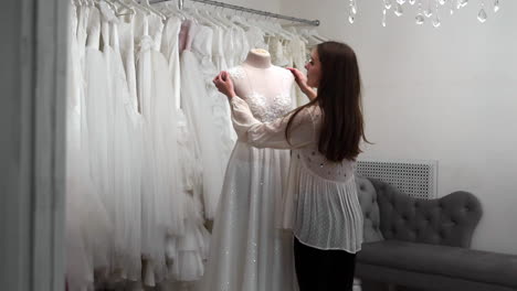 hermosa niña buscando vestido de novia en la cabina en comparación con otros vestidos. preparando para la boda. comprando un vestido de novia. la costurera inspecciona el vestido de novia hecho a medida terminado.