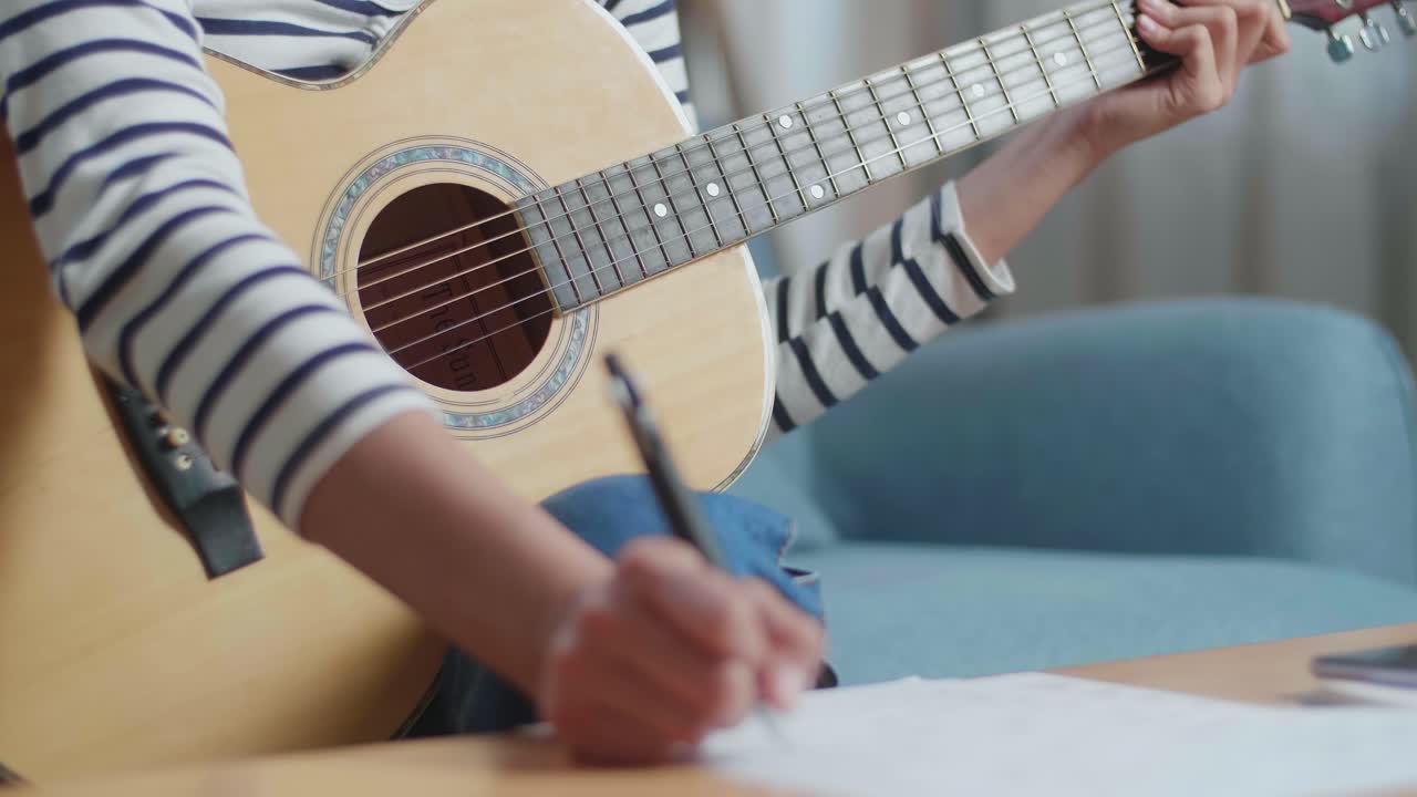 близкий взгляд на азиатскую композиторку, сочиняющую музыку на бумаге и играющую на гитаре дома.