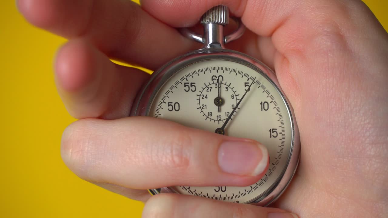 la mano de una mujer sostiene un cronómetro analógico sobre un fondo amarillo.