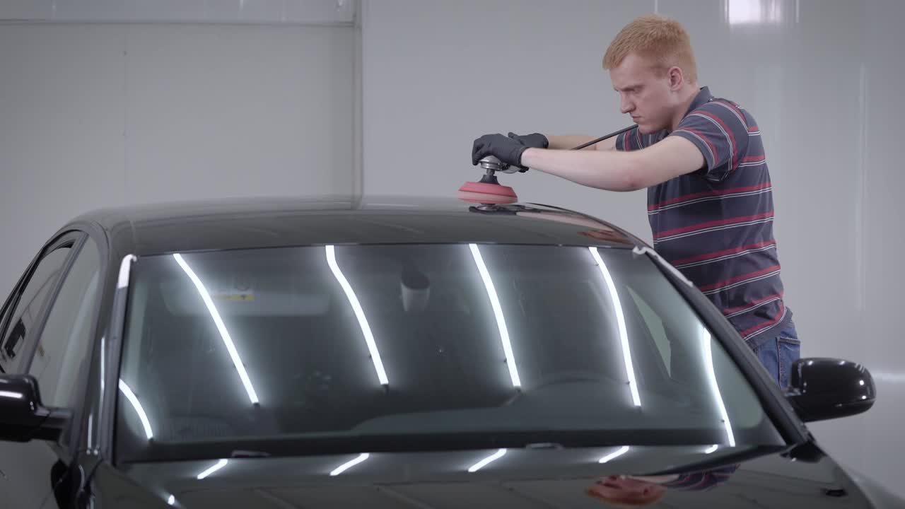 차고 에 서 있는 성인 남자 의 측면 시상 과 자동차 지붕 에 있는 폴리싱 기계 를 사용 하는 것