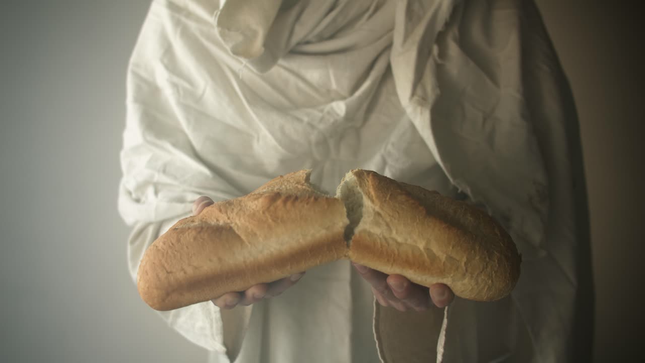 Closeup of Jesus Christ in white robe breaking bread in ambient glowing light. Perfect for Christianity Easter visual, gospel symbolism of Jesus as the bread of life.