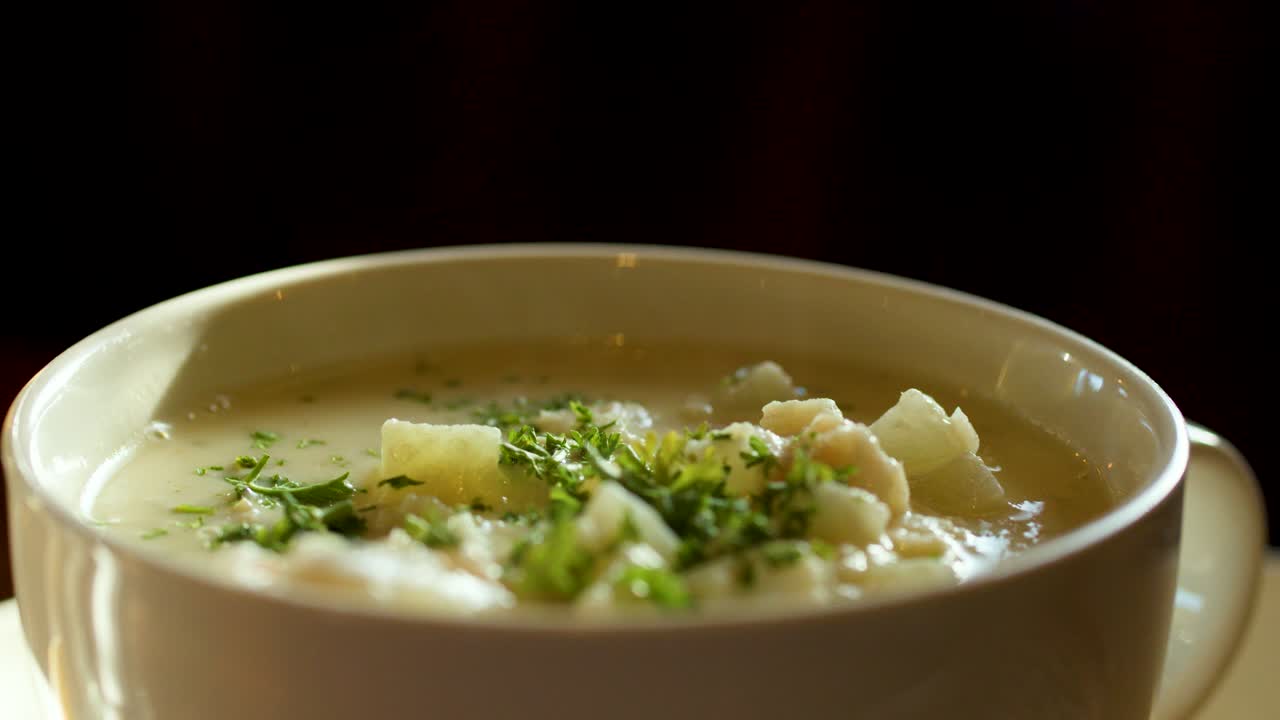 Close-up of creamy chowder garnished with herbs, warm natural lighting, slight camera movement, inviting mood