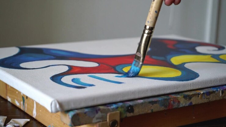 Abaixando o pincel, mão do artista adicionando pinceladas azuis em tela sobre a mesa, preenchendo a forma com suporte de madeira.