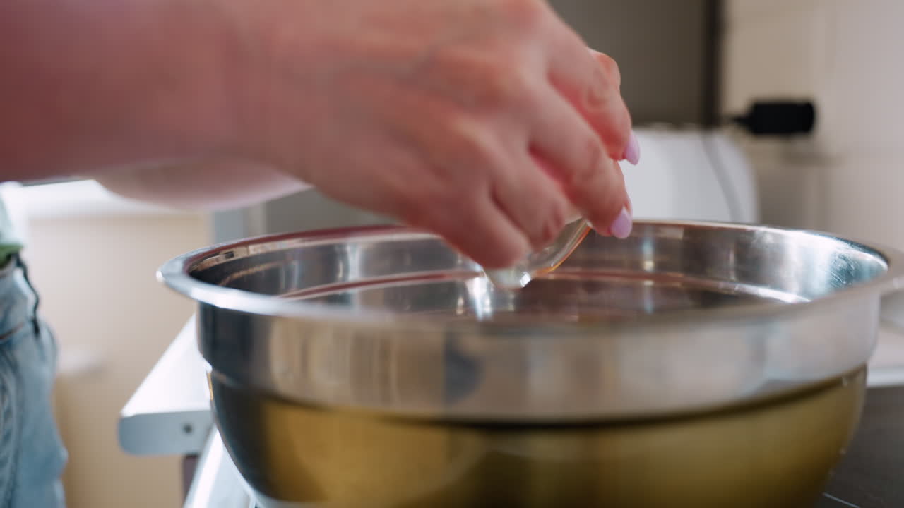 Close up of woman hand cracking fresh egg into stainless steel mixing bowl in kitchen, preparing ingredients for cooking with natural light