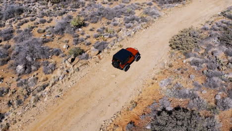 Aerial-of-Orange-Off-Road-Vehicle-Driving-on-Dirt-Road-through-Desert-Mountains---Slow-Speed