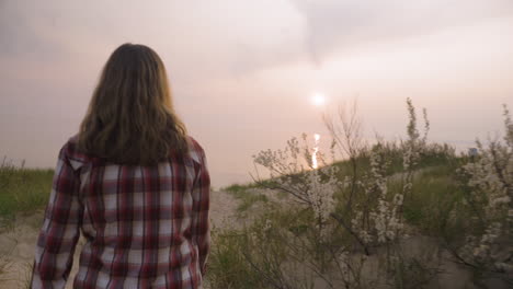 disparo de mano siguiendo a una mujer joven caminando a lo largo de una playa de arena al atardecer