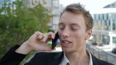 happy young caucasian man talking on phone outside, smiling