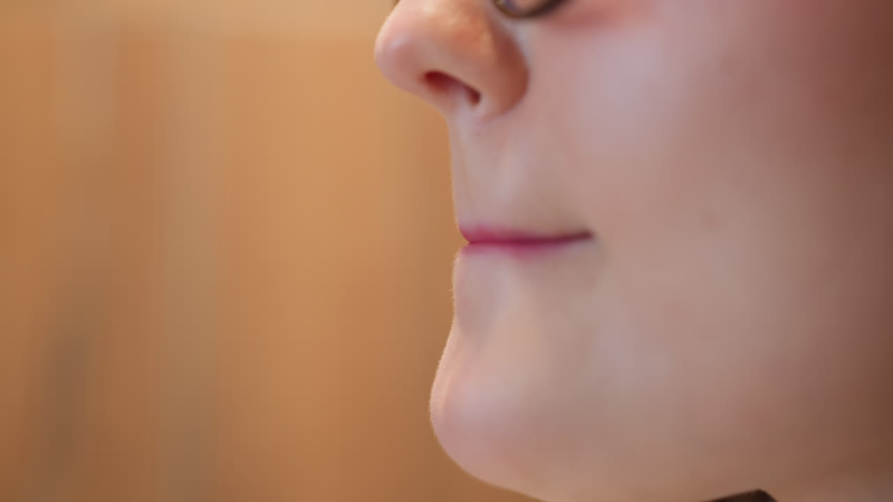 side view close up of woman applying lipstick with intense focus, hand holding cosmetic tube near lips, soft lighting highlights skin texture and delicate gesture in relaxed indoor environment