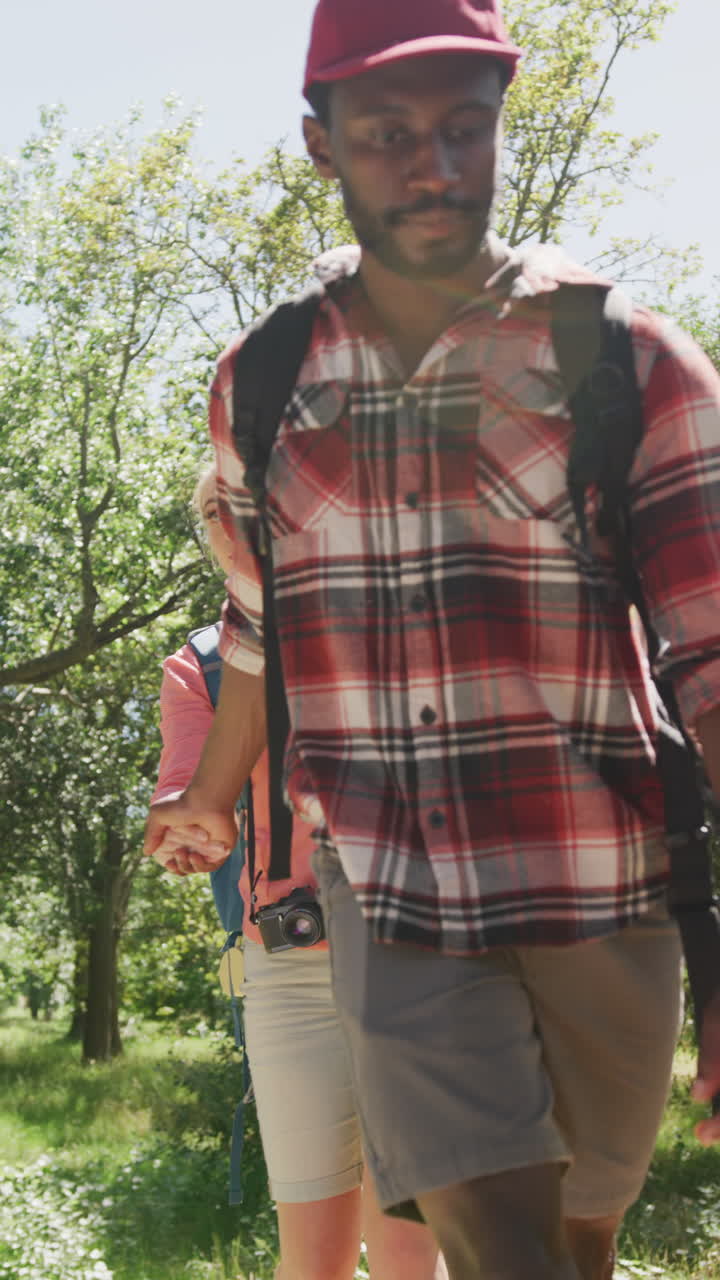 Vertical video of happy diverse couple hiking in park, slow motion