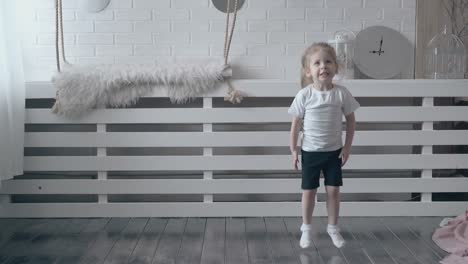 little blond girl with pigtail jumps on wooden floor