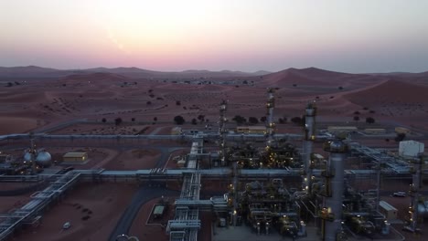 aerial view of an oil extraction facility at sunset surrounded by serene desert landscapes with distant hills and a colorful evening sky