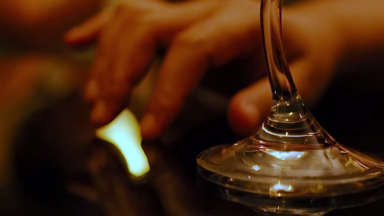 Close-up of fingers interacting with the base of a wine glass on a reflective surface.