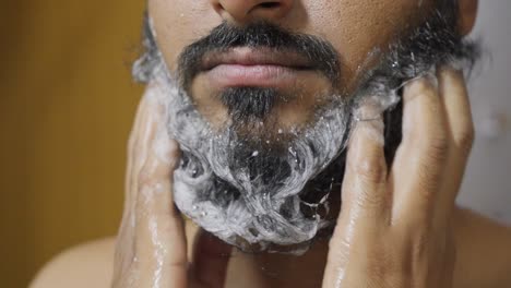 a close-up footage of a south asian man rubbing his beard with soap and water, with a blurred background