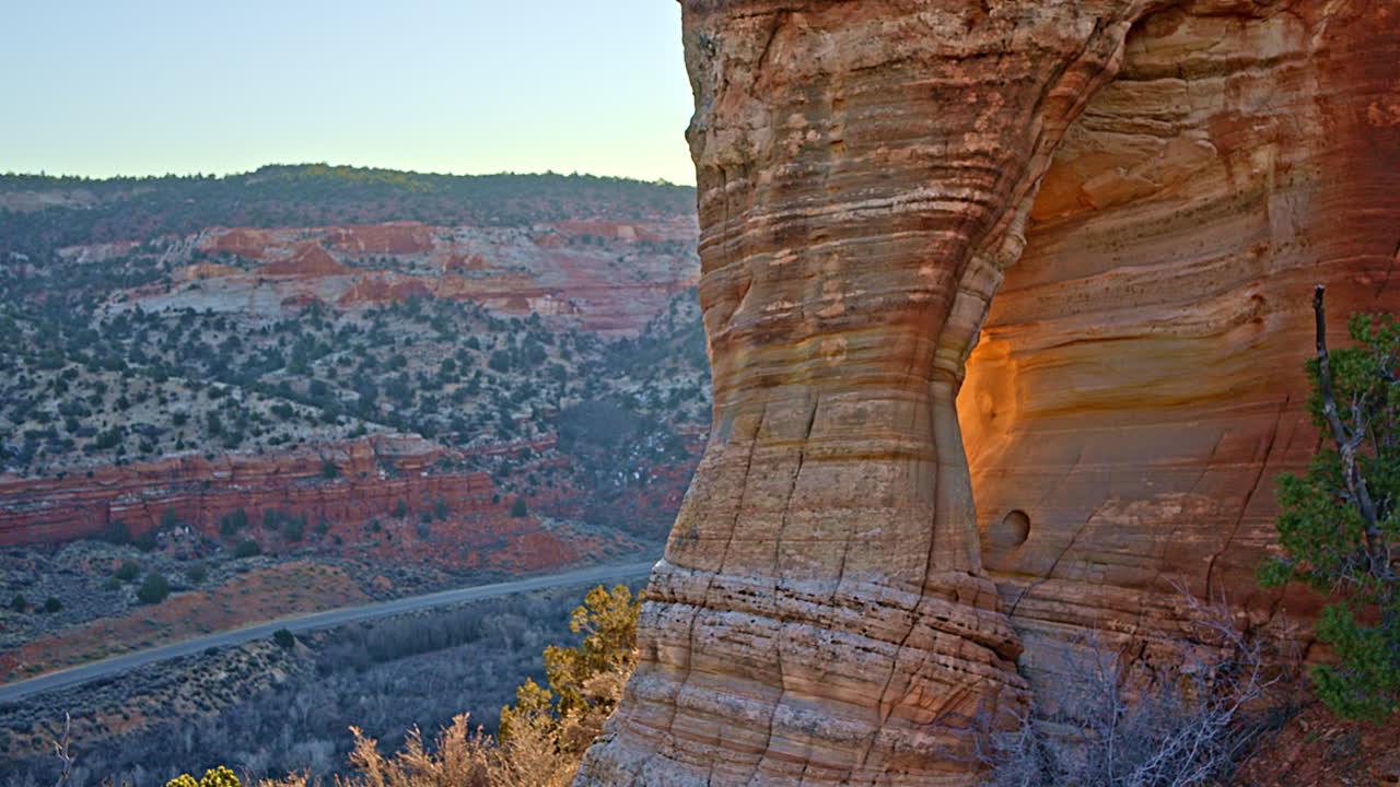 Drone shot flying over a picturesque natural arch in Utah’s rugged red rock terrain at sunrise.