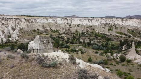 a woman with a dress standing on the viewpoint on love valley, drone zoom out the picturesque landscape of cappadocia, turkey