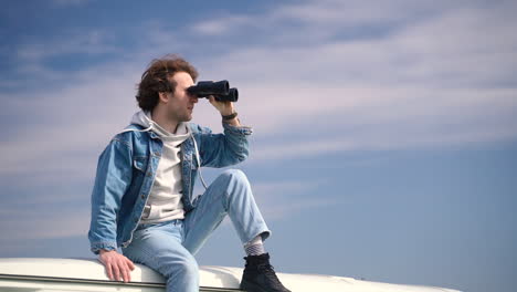 young boy looks around with a pair of binoculars on the roof of a caravan