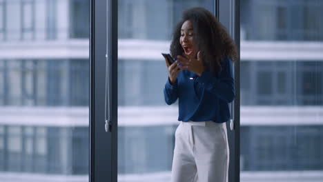 Excited-african-american-manager-woman-celebrating-good-news-on-phone-in-office.