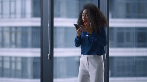 excited african american manager woman celebrating good news on phone in office.