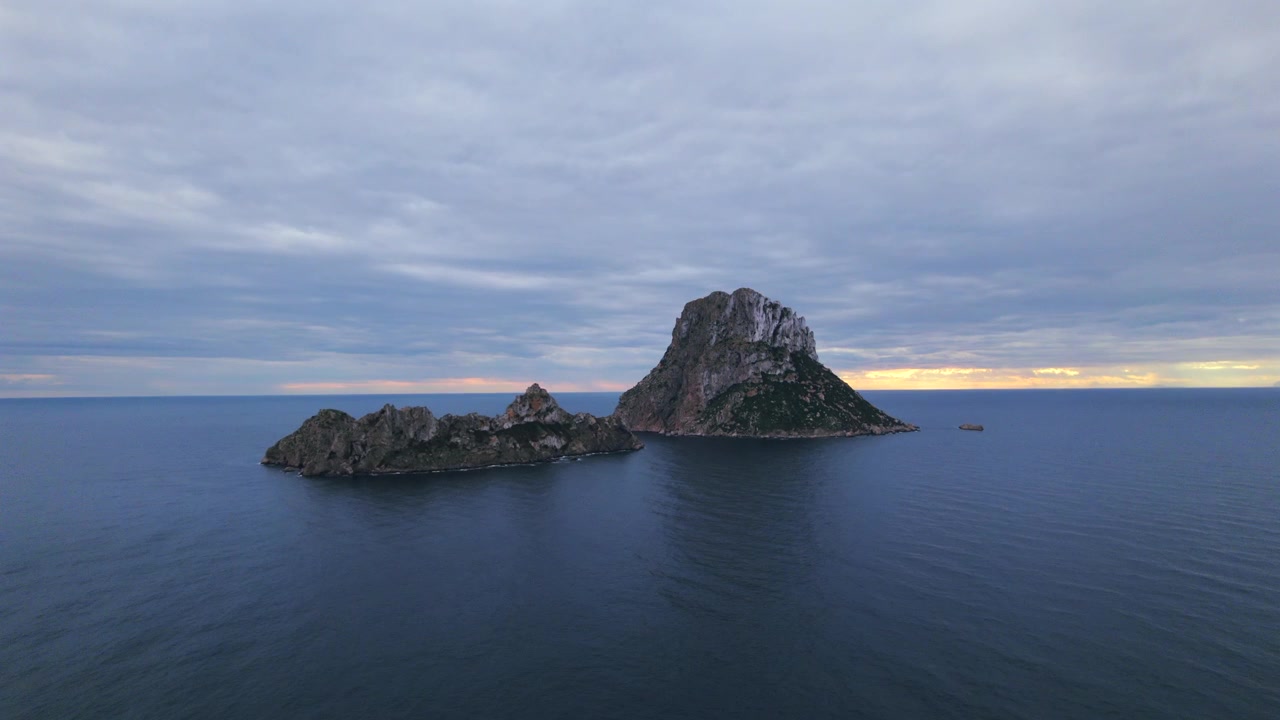 Ripresa aerea in 4K con drone di Es Vedrà al tramonto, Ibiza, Spagna. L'iconica isola rocciosa emerge dal Mar Mediterraneo mentre una calda luce dorata illumina la costa e le acque circostanti