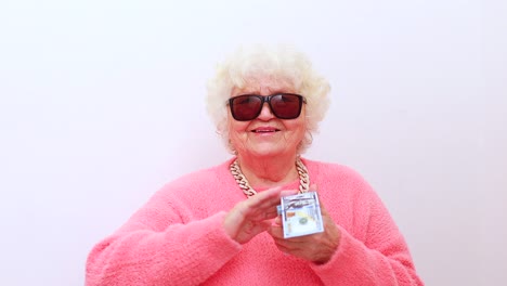 una anciana rubia lleva un suéter rosado y gafas de sol lanzando dinero aislado fondo blanco