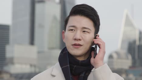 joven empresario asiático hablando por teléfono móvil con el horizonte de la ciudad de londres en el fondo 1