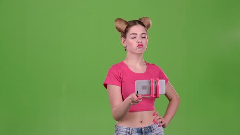 young woman posing for selfies with a selfie stick on a green screen