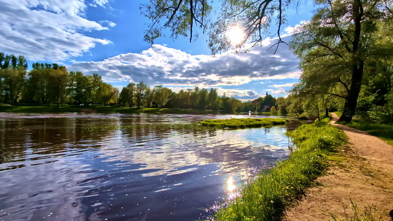 Riverbank footpath under bright sky and sun with trees reflecting in water of Gauja river
