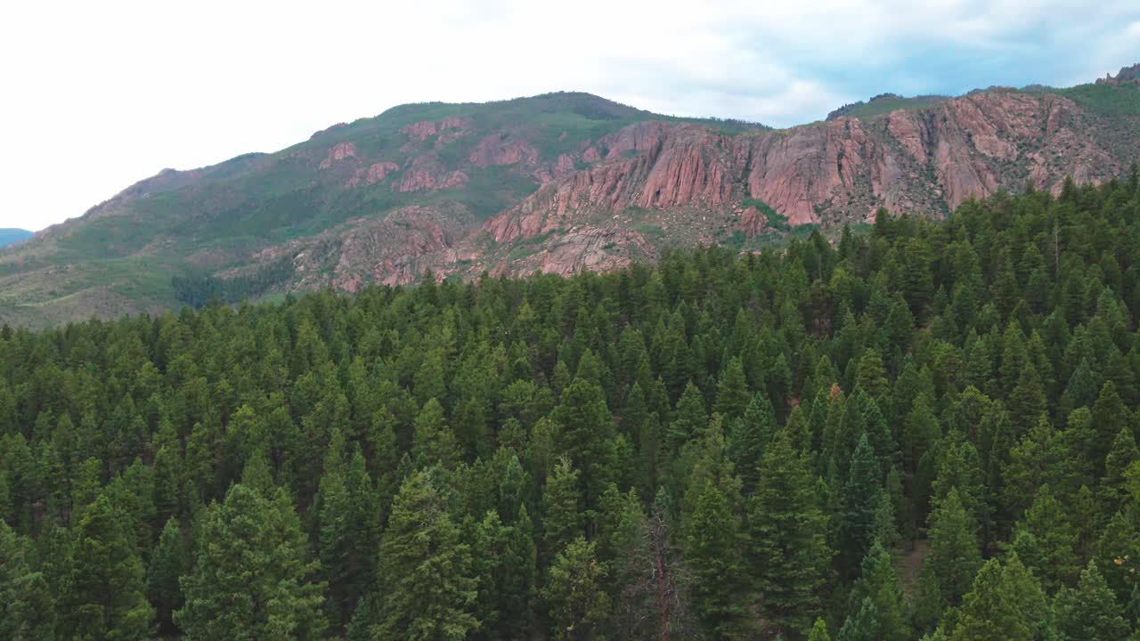 Aerial view approaching remote red cliffs over a pine forest. Filmed with a drone in the Pike National Forest
