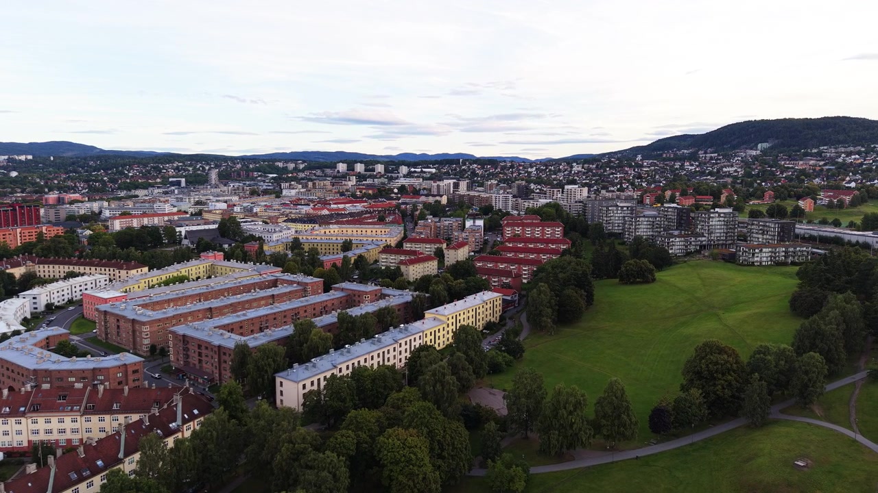 Fargerike leilighetsblokker i Oslo grenser til et bredt grønt fellesområde mens en drone flyr sakte over boligområdet.