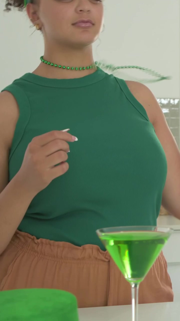 Video verticale: Mentre solleva delle perline, una donna in verde che si mette una collana in cucina vicino a dei cocktail, spazio per il testo