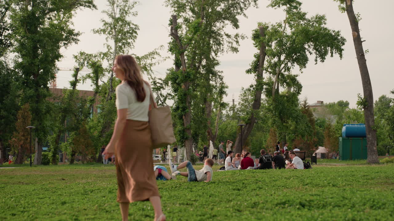 back view woman walking in park admiring playful child running ahead on green grass, warm light, casual outfit, peaceful recreation moment, blurred trees background, summer family outing
