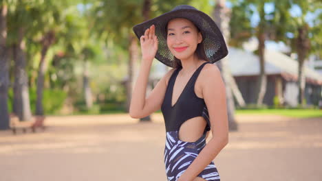 a pretty asian woman in her bathing suit moves in the frame as she adjusts her floppy sun hat