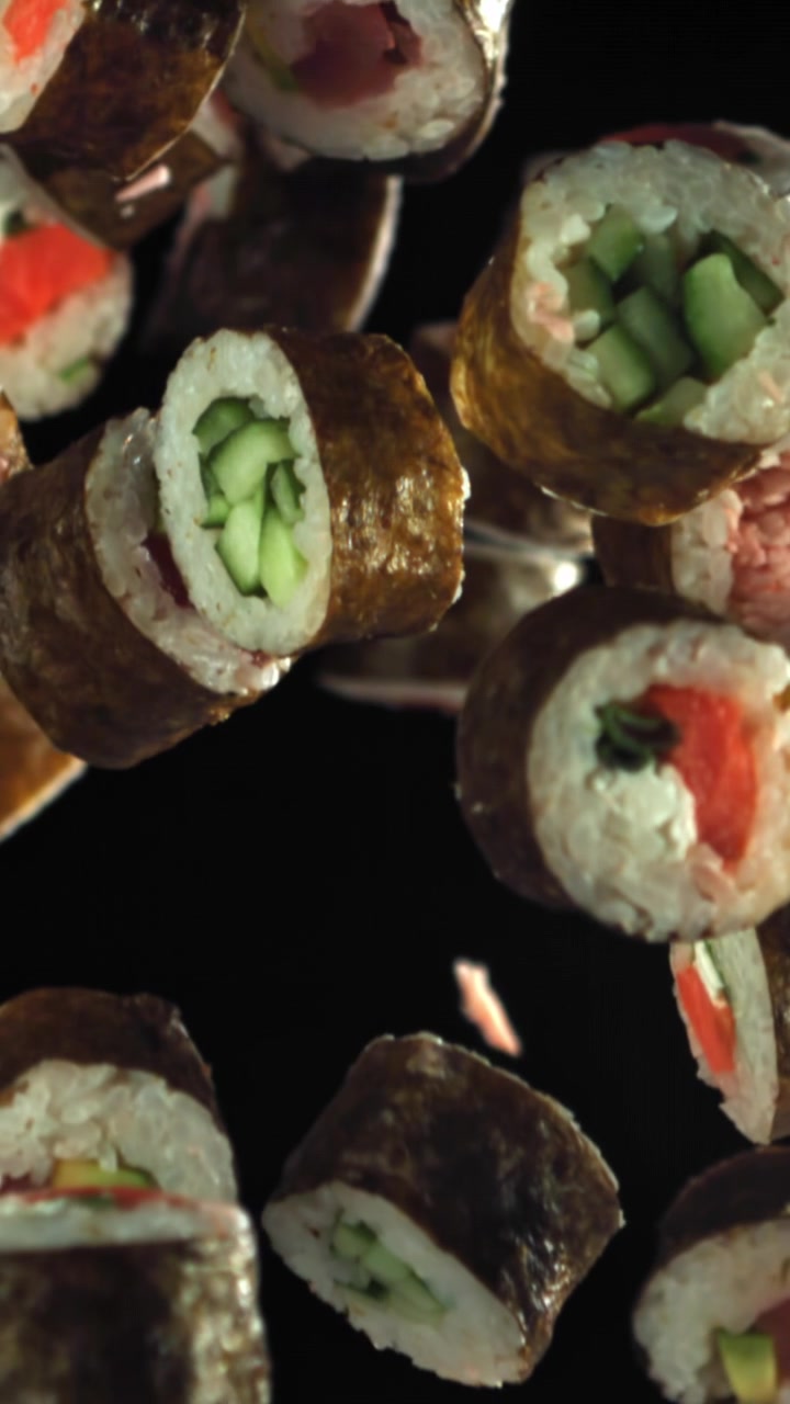 Vari rotoli di sushi che cadono al rallentatore su sfondo nero