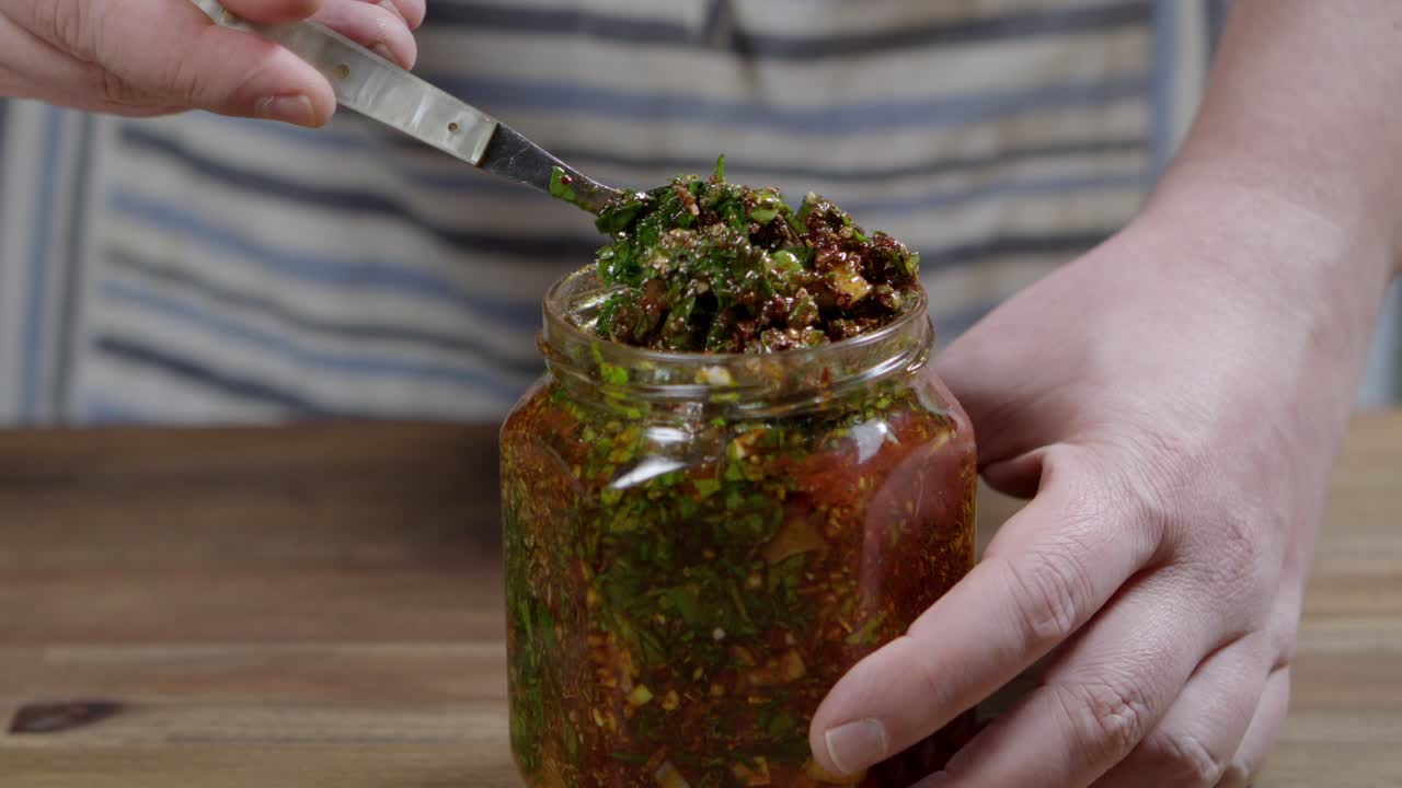 persona que agita la salsa de chimichurri en un frasco