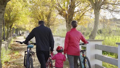 family, parents and children, walking along a path with their bikes on a sunny day