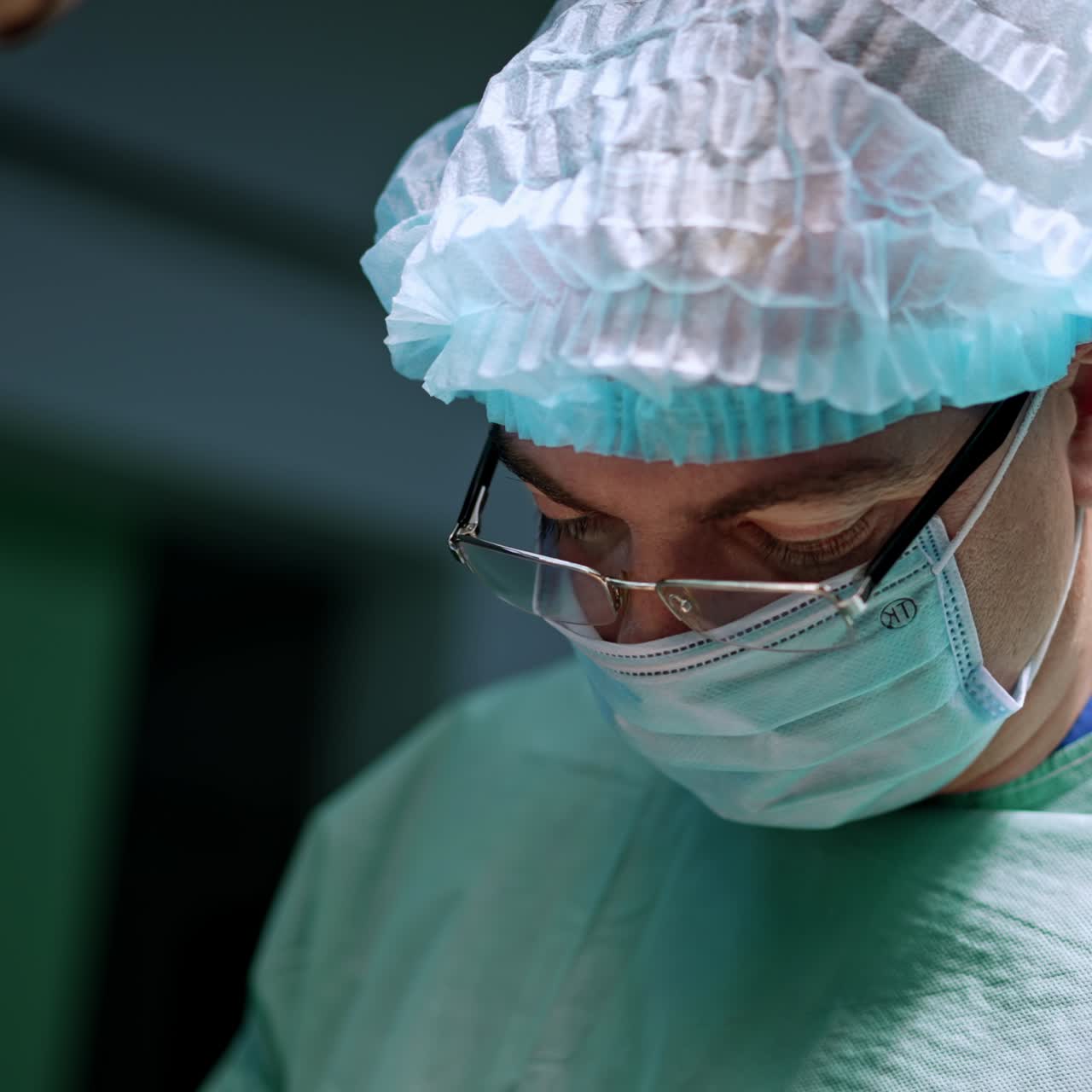 Portrait of a busy male adult surgeon. Medic is wearing eyeglasses, cap and mask performing operation. Close up