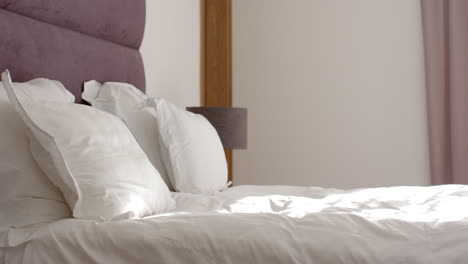 A-neatly-made-bed-with-white-linens-is-in-focus,-with-a-purple-headboard,-with-copy-space