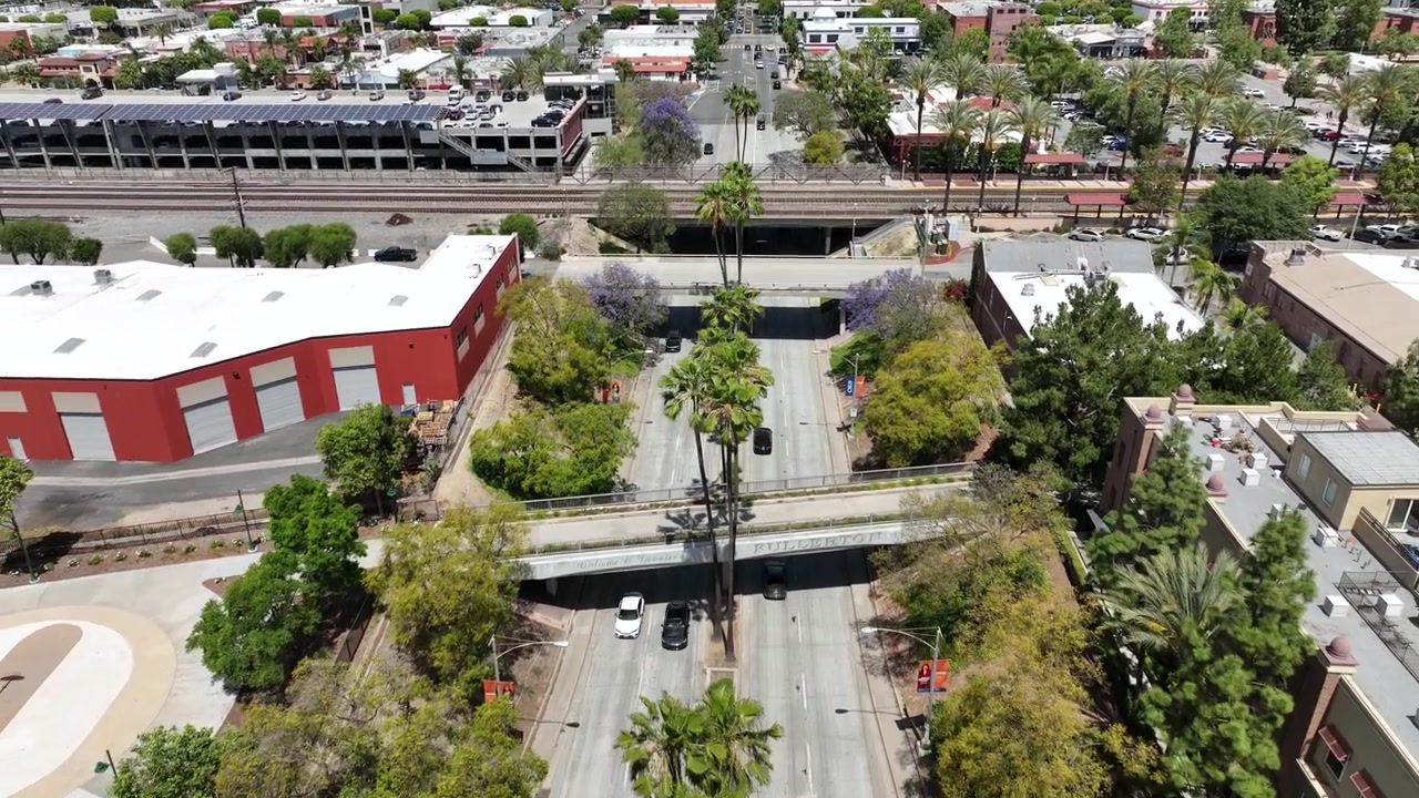 Riprese aeree del centro di Fullerton, California, che mostrano il traffico di Harbor Boulevard, le strutture dei cavalcavia ferroviari e un treno passeggeri che attraversa il paesaggio urbano.