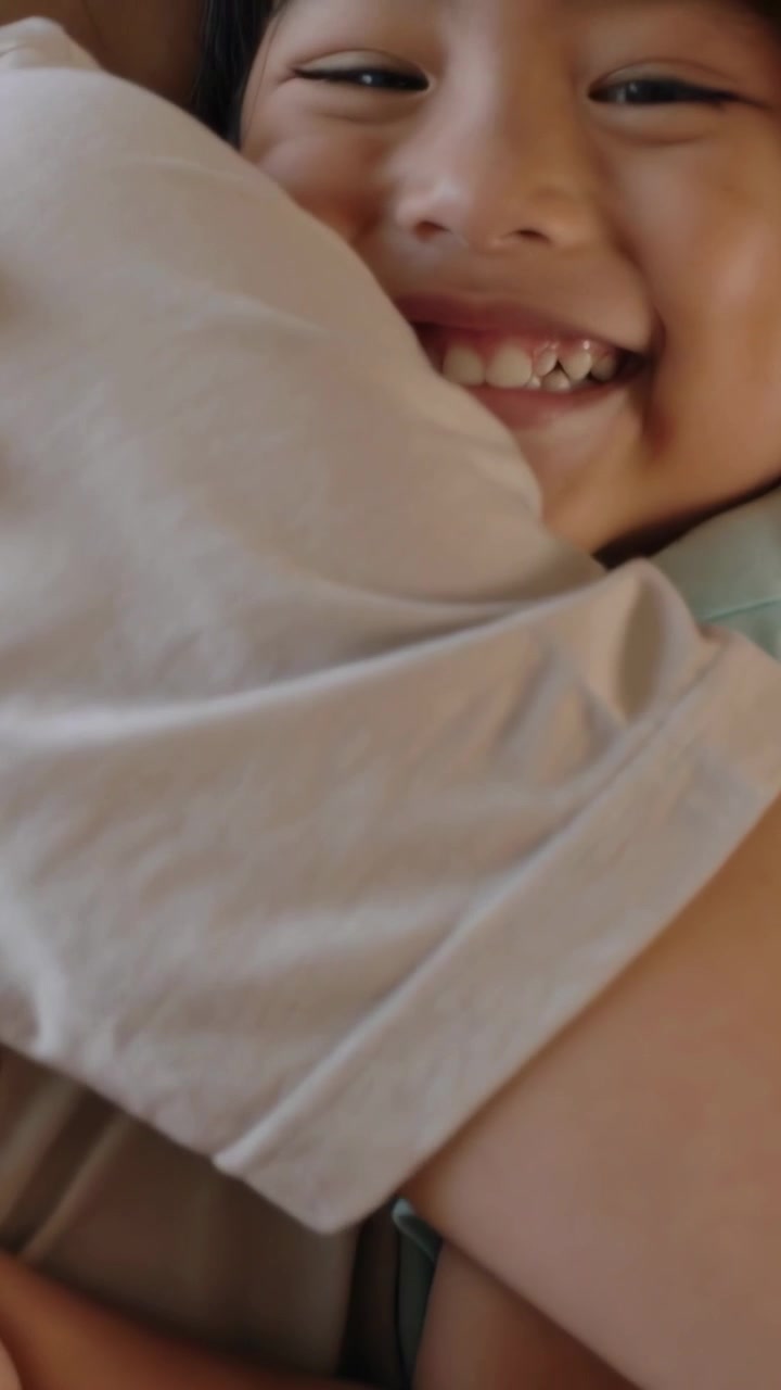Video verticale: Un adulto che abbraccia e tiene in braccio un bambino sul divano, con il bambino che sorride ampiamente per il comfort, indossando una maglietta color menta.