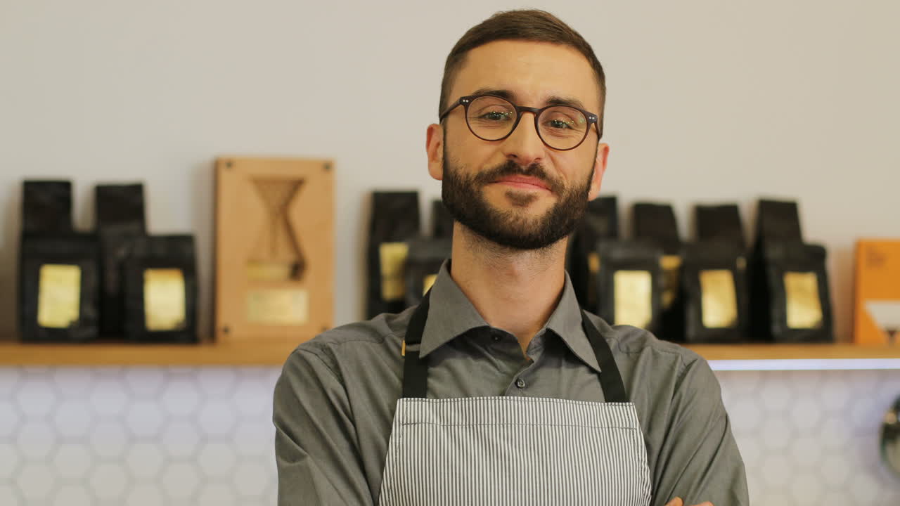vista de primer plano de un feliz barista masculino con anteojos en la cafetería posando y sonriendo a la cámara