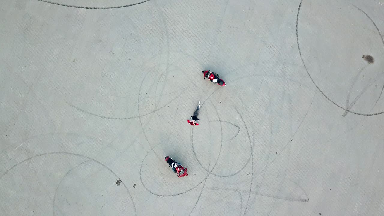 Top view of two professional bikers racing slowly in a circle way. Young woman is lying in the middle of a road and two motorcycles riding around her. Dangerous sport. Aerial view.
